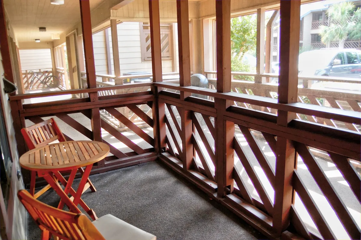 An inviting screened porch with wooden railing, two comfortable chairs, and a small table. The tranquil setting suggests a private spot for two to relax, enjoy a glass of wine, or reflect on the day’s adventures.