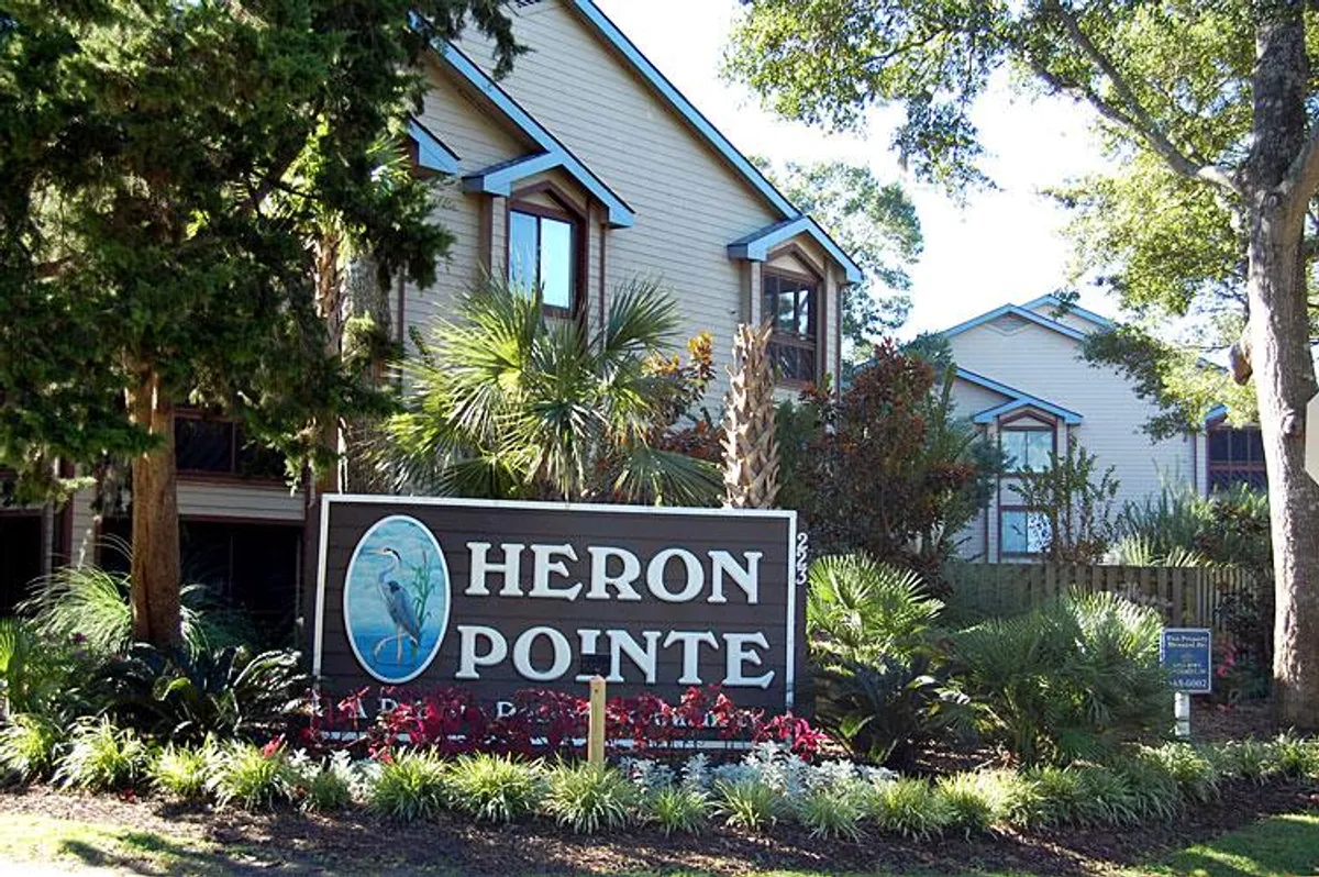 This image showcases the welcoming Heron Pointe signage set amidst lush landscaping and the residential buildings. The scene hints at a tranquil and friendly resort environment, ideal for groups and families arriving or gathering to begin their adventures together. The residential setting subtly suggests the communal and multi-generational appeal referenced in the section.
