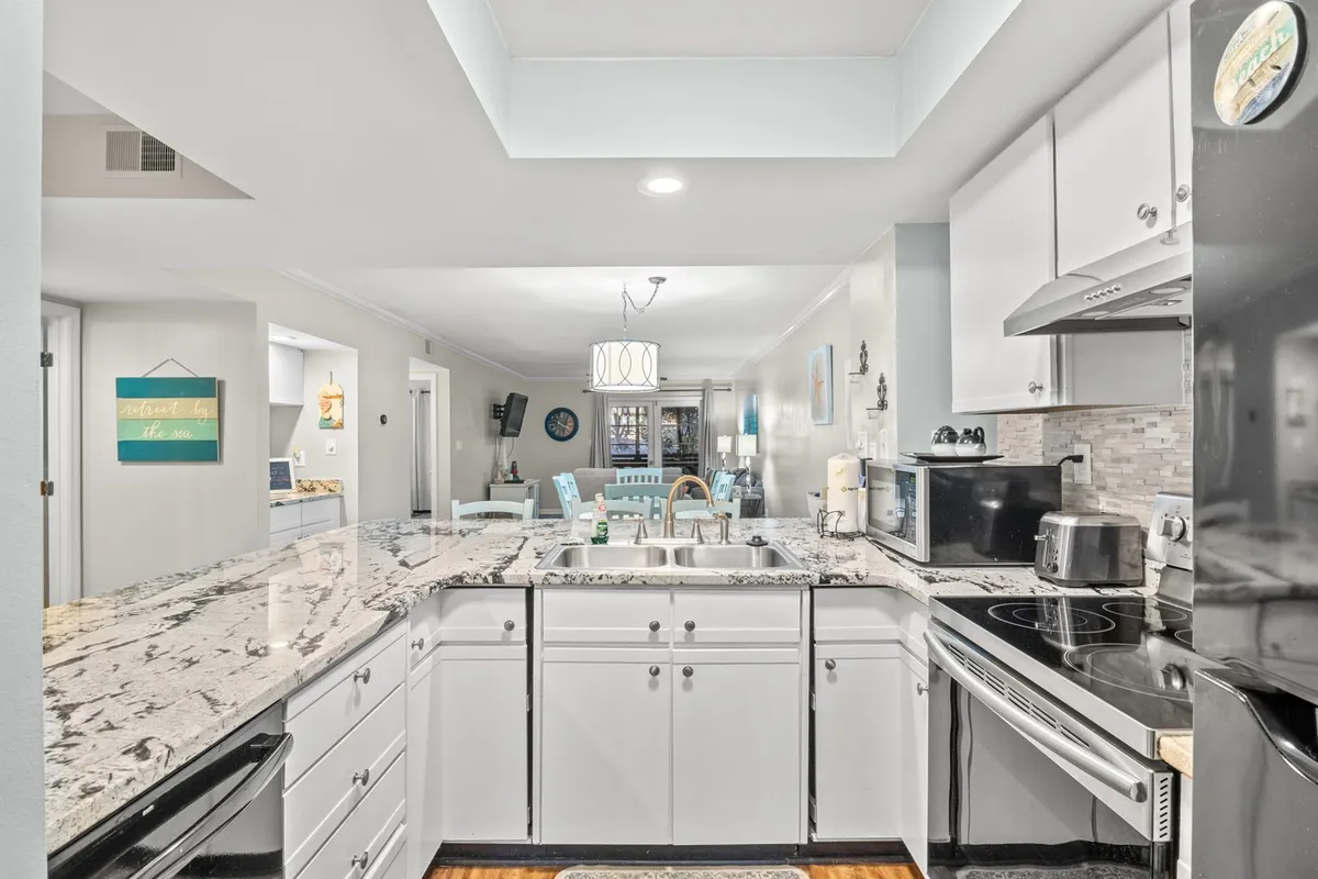 A warmly lit kitchen with granite countertops, stainless steel appliances, white cabinetry, and an open layout that flows into the dining area. The scene exudes a welcoming and social atmosphere, perfect for gathering and sharing meals.