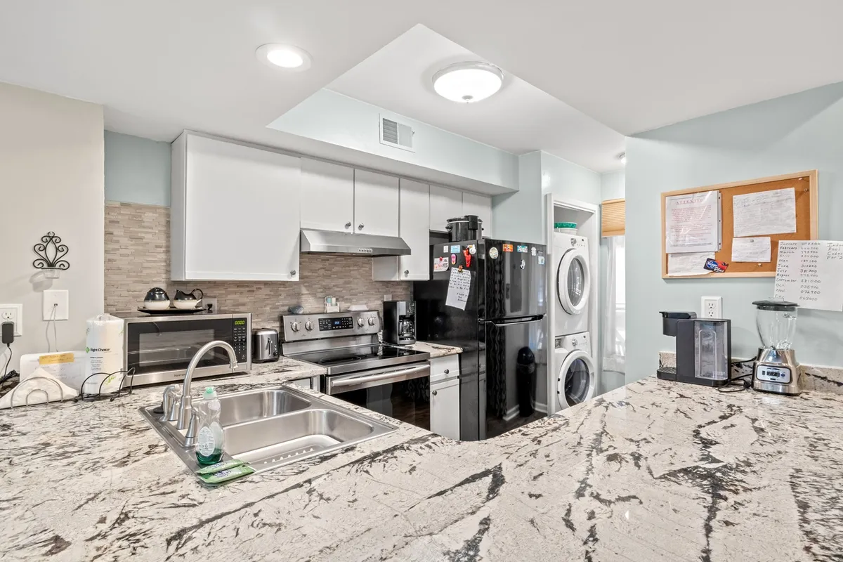 This image features a modern kitchen with a granite countertop, stainless steel appliances, a black refrigerator, and an adjacent laundry area. The layout is inviting and practical, with spacious counters ideal for meal preparation.